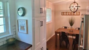 A kitchen with white cabinets, a wooden countertop, a dining table with chairs, a refrigerator, and a 'GROCERY' sign on the wall. - Convenient 3 Bedroom / 2 Bath house (Gainesville)
