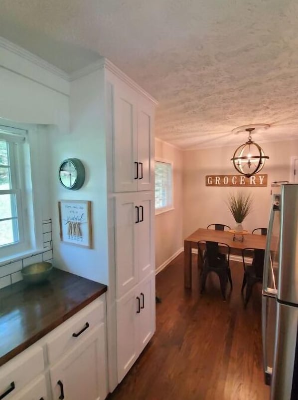 A kitchen with white cabinets, a wooden countertop, a dining table with chairs, a refrigerator, and a 'GROCERY' sign on the wall.