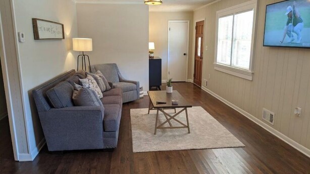 A living room with a grey sofa, a coffee table, and a TV mounted on the wall. - Convenient 3 Bedroom / 2 Bath house (Gainesville)