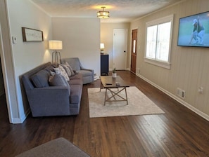 A living room with a grey sofa, a coffee table, and a TV mounted on the wall.