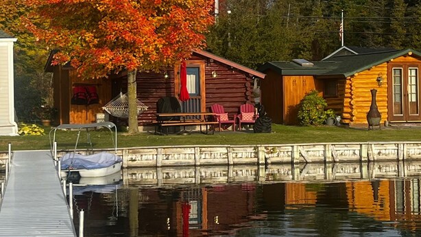 Une cabane avec un quai et un grand arbre aux feuilles d’automne.