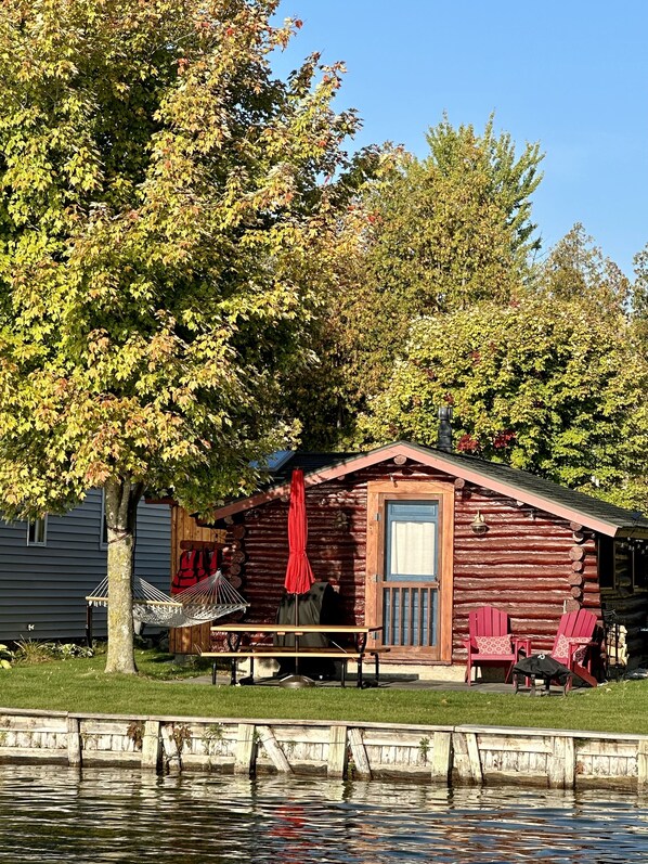 A log cabin with a dock, a hammock, and a small table with chairs.