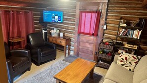 L’intérieur chaleureux d’un chalet en bois comprend un fauteuil en cuir, une table en bois, un canapé, un téléviseur fixé au mur et une bibliothèque remplie de livres.