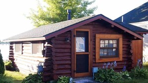 Une cabane en rondins avec une porte et une fenêtre en bois, entourée de verdure.