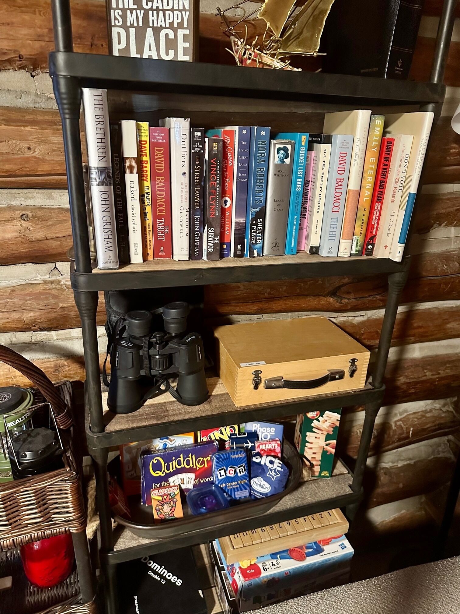 Ein Bücherregal mit verschiedenen Büchern, zwei Spielecontrollern und einem Karton.