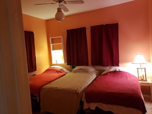 A hotel room with two beds, a ceiling fan, a window with curtains, and a bedside lamp.