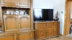 Een houten kast met een flatscreen televisie erboven, een vaas met decoratieve takken en een houten vloer.