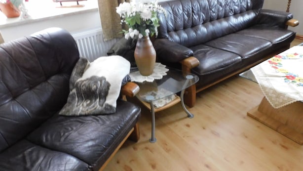 Een woonkamer met een zwarte leren bank, een klein glazen bijzettafeltje en een vaas met bloemen.