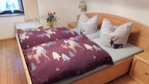 Een houten bed met een paars dekbed met dierenprint, witte kussens en een klein nachtkastje met een lamp.