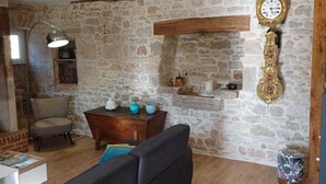 Una sala de estar acogedora con una pared de piedra, techo con vigas de madera, un reloj grande y una chimenea.
