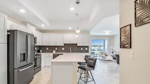 Cocina moderna con una isla central, taburetes de bar y vistas al área de estar.