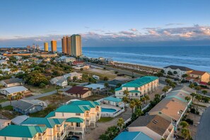 A coastal residential area with houses featuring green roofs, a beach, and high-rise buildings in the background. - Stay Salty (Panama City Beach)