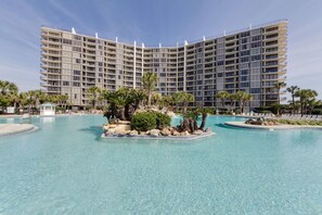 A large hotel with multiple balconies and a central pool area with palm trees and rocks. - Edgewater Tower 2 Unit 505 (Panama City Beach)