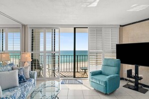 A balcony with a view of the sea, a sofa, a chair, a TV, and a glass table. - Edgewater Tower 2 Unit 505 (Panama City Beach)