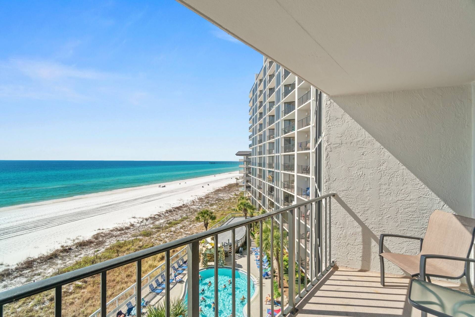 A balcony with a view of a beach and a swimming pool.
