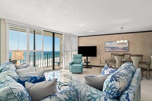 A spacious living room with a large sofa, a small table, and a chair. There is a balcony with a view of the beach. - Edgewater Tower 2 Unit 505 (Panama City Beach)