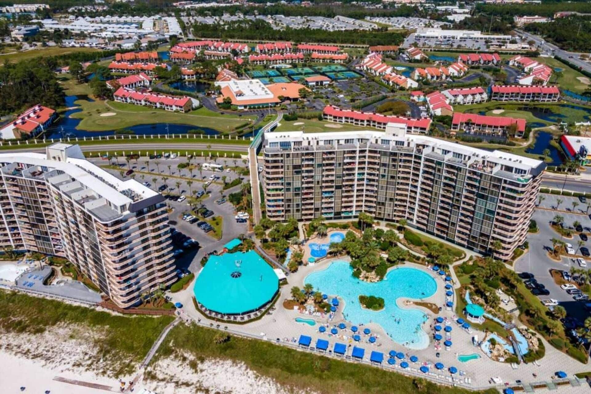 A high-rise hotel with multiple balconies, a central swimming pool, and surrounding resort buildings.