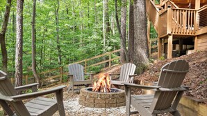 Eine bewaldete Freifläche mit Feuerstelle und Adirondack-Stühlen.