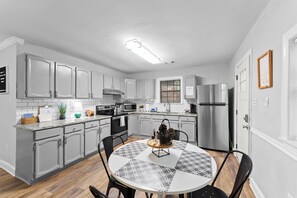 A modern kitchen with grey cabinets, a stainless steel refrigerator, and a dining area with a patterned table and chairs.