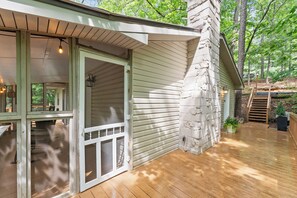 A wooden deck with a stone chimney, a covered porch, and a view of the surrounding forest.