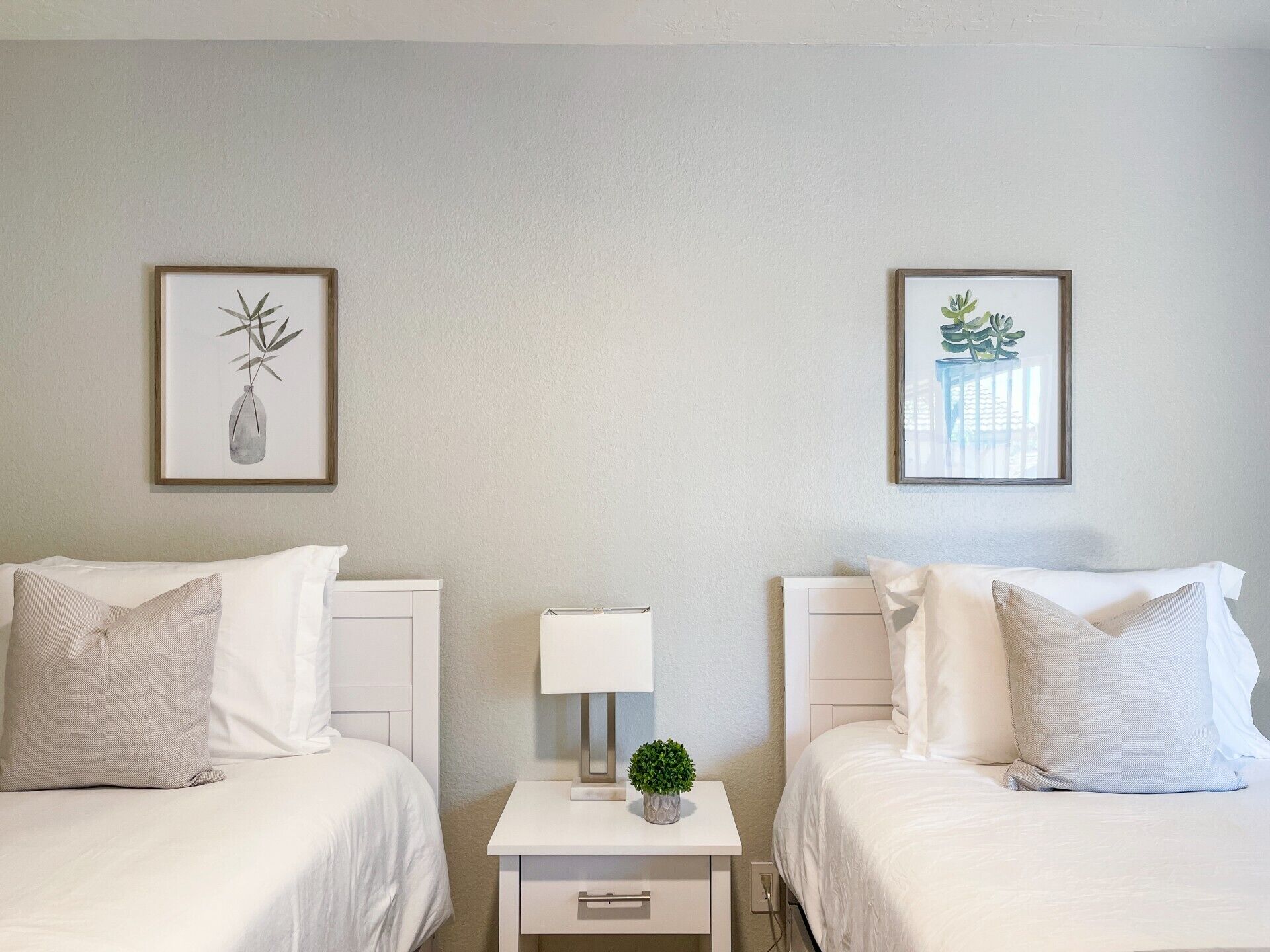Een hotelkamer met twee bedden, een nachtkastje met een lamp en twee ingelijste foto's aan de muur.