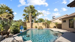 A swimming pool with clear water, surrounded by palm trees and a deck with lounge chairs.