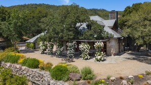 A rustic stone building with a sloped roof, surrounded by a garden with flowering plants and a stone wall. - Magnificent Estate, Vineyard Views, Pool and  Spa - Sonoma Valley Farm Stay (Sonoma)