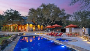 A pool area with lounge chairs and umbrellas, surrounded by trees and a building with outdoor lighting. - Magnificent Estate, Vineyard Views, Pool and  Spa - Sonoma Valley Farm Stay (Sonoma)