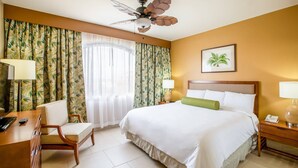 Habitación de hotel con cama, escritorio, silla, ventilador de techo y un cuadro en la pared.