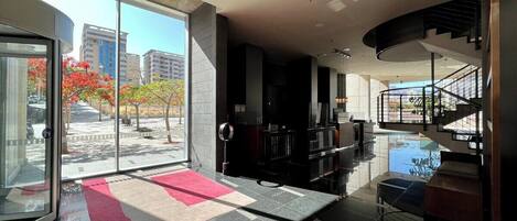 A spacious lobby with a glass door leading to an outdoor area, a staircase, and a reception desk.