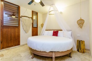 Ein Schlafzimmer mit einem runden Bett, Holztür, Deckenventilator und einer Wanddekoration.
