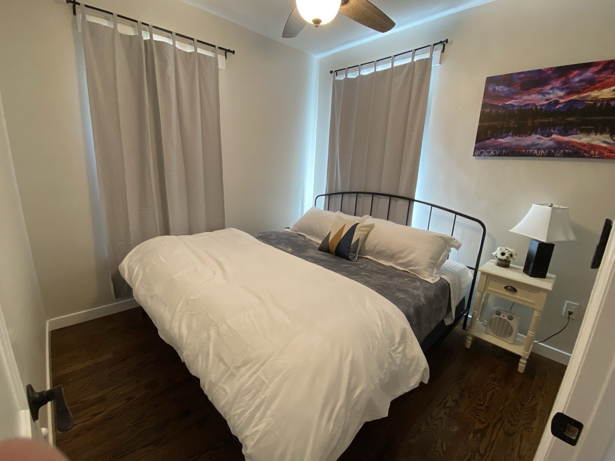 Une chambre à coucher avec un lit, des rideaux, une table de chevet avec une lampe et un tableau au mur.