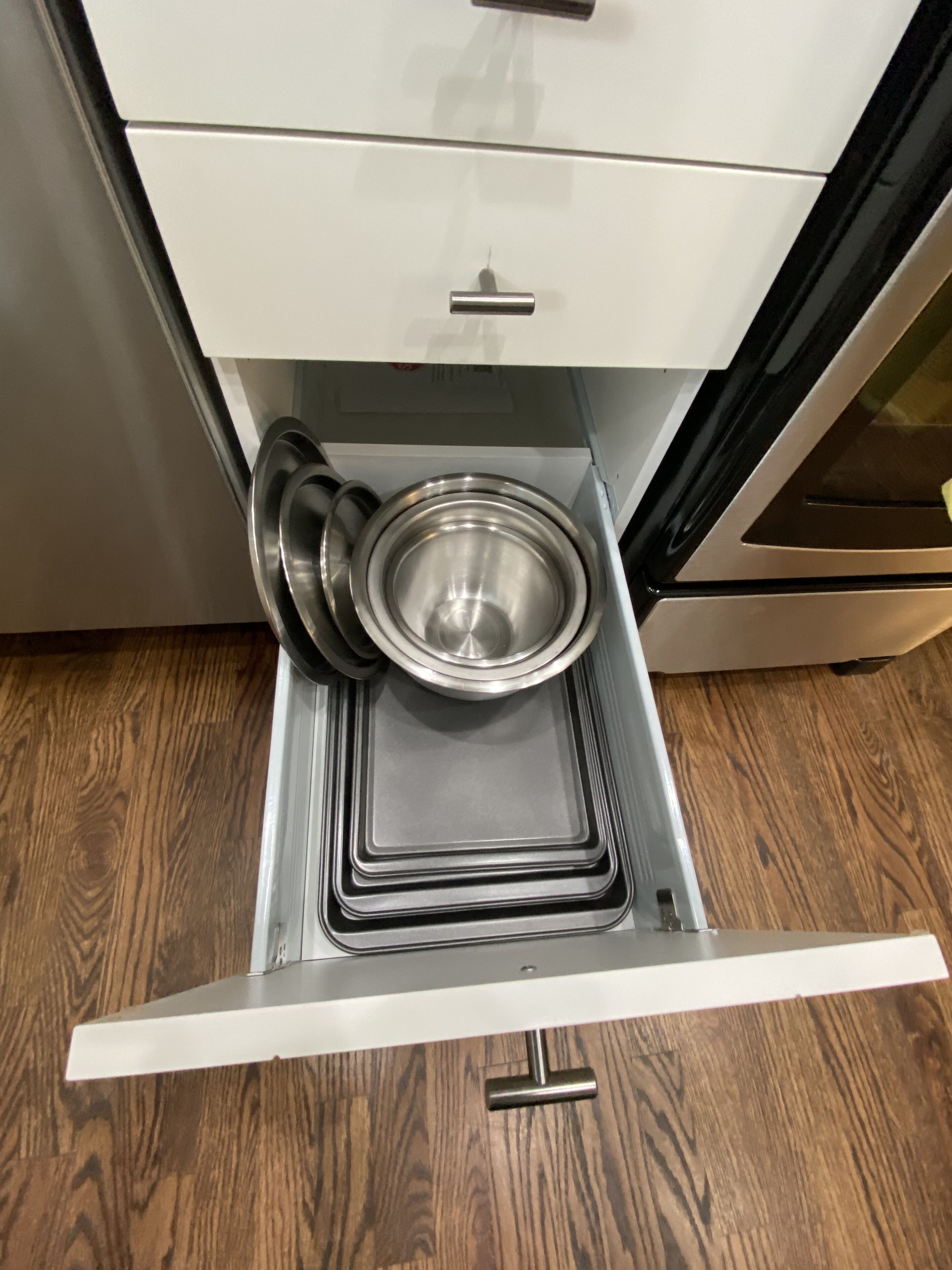 Una cocina con un lavamanos de acero inoxidable, una encimera blanca y suelo de madera.