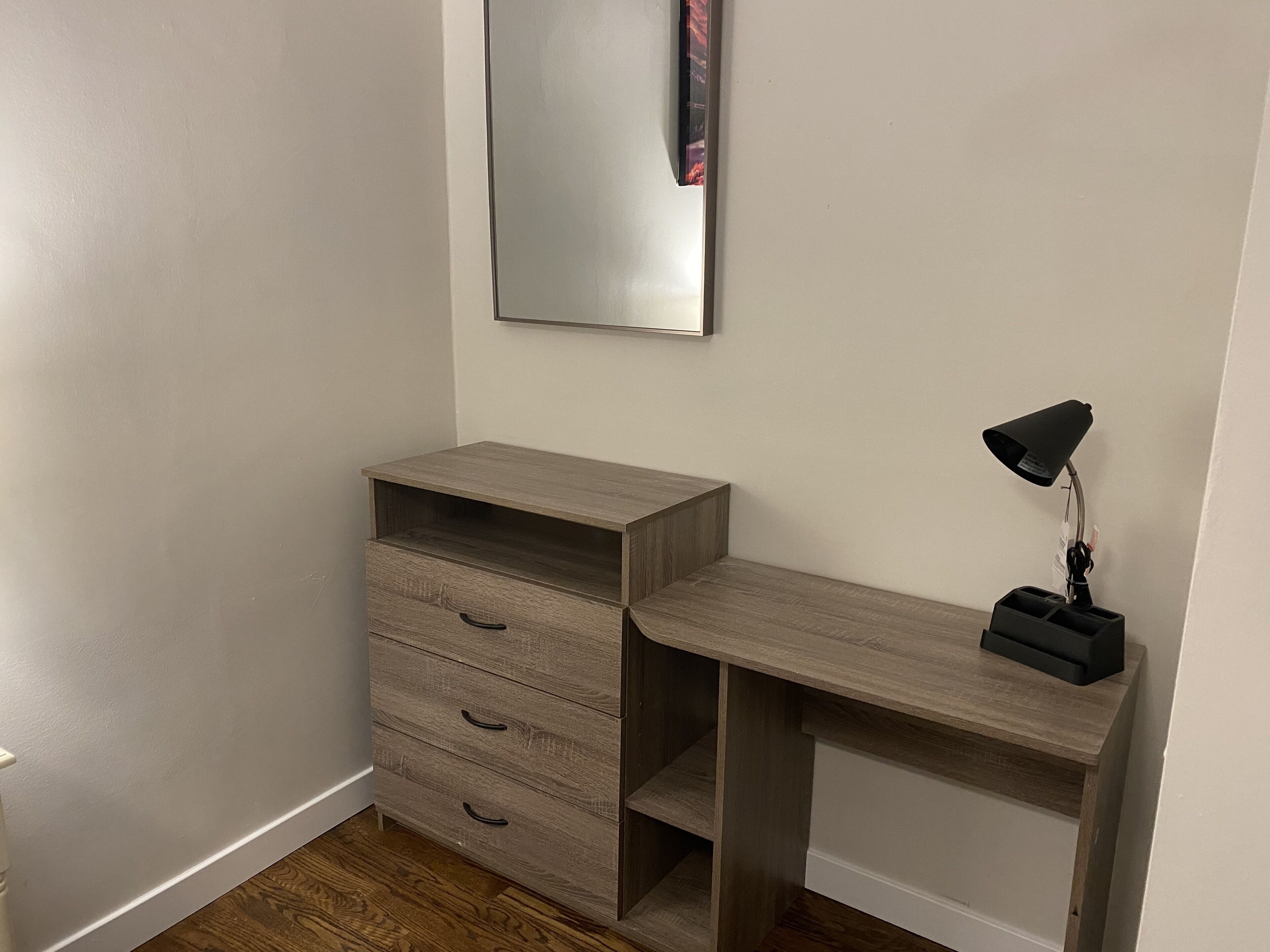 A corner room with a wooden desk, a mirror, and a desk lamp.