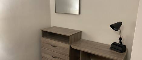 A corner room with a wooden desk, a mirror, and a desk lamp.