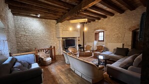 A rustic living room with stone walls, wooden beams, and a fireplace. There are several sofas and chairs arranged around a central coffee table. - Large gite sleeps 23 with all comforts (Lalandusse)