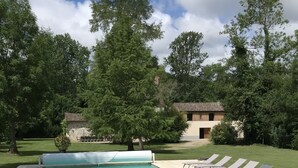 A rectangular swimming pool with a tiled deck, surrounded by lounge chairs and a grassy area with trees. - Large gite sleeps 23 with all comforts (Lalandusse)