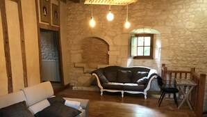 A cozy living room with a stone wall, a fireplace, a sofa, a coffee table, and a chair. - Large gite sleeps 23 with all comforts (Lalandusse)