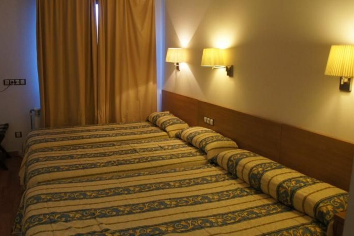 Habitación de hotel con una cama grande, dos lámparas de pared, un televisor y una ventana con cortinas.