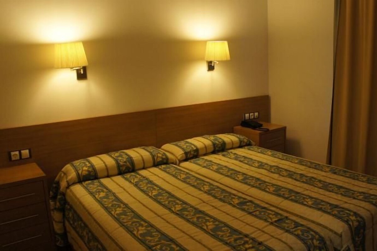 A hotel room with a bed, bedside tables, lamps, and a curtain.