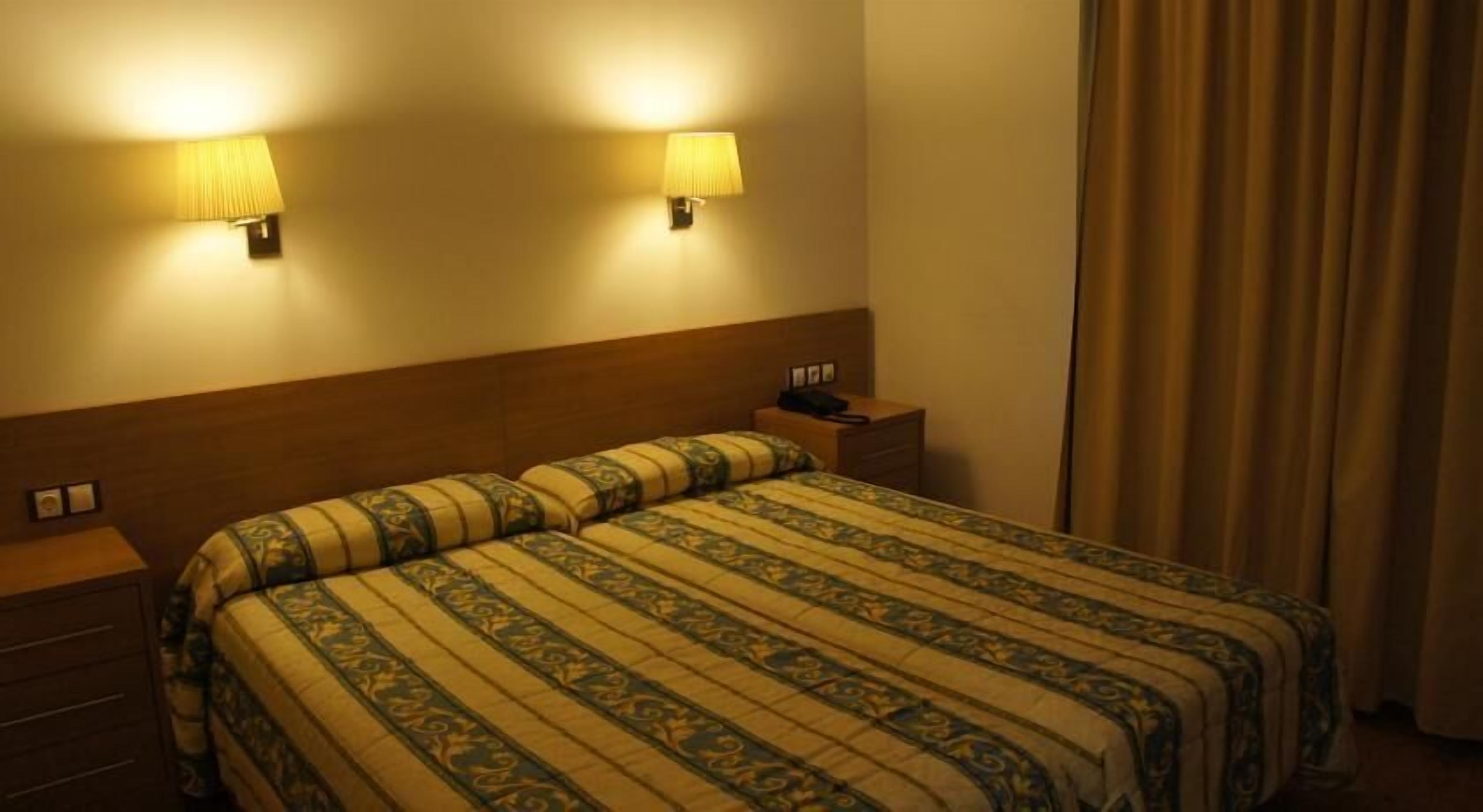A hotel room with a bed, bedside tables, lamps, and a curtain.