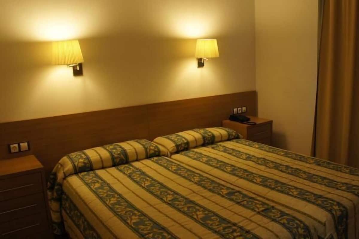A hotel room with a bed, bedside tables, lamps, and a curtain.