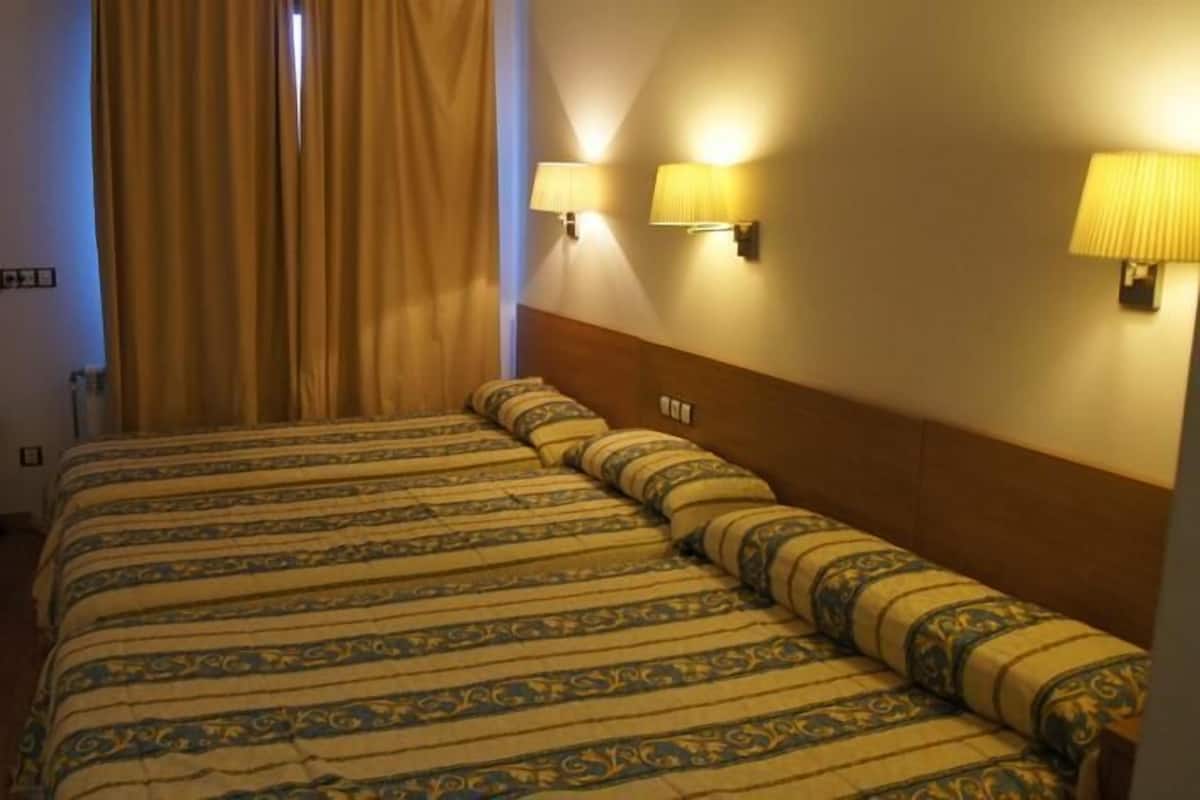 A hotel room with a large bed, two wall-mounted lamps, a TV, and a window with curtains.