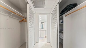 A narrow hallway with a closet on the right, a wooden hanger rod on the left, and a door leading to a bathroom. - Comfortable Apartment steps away from the beach (Hollywood)