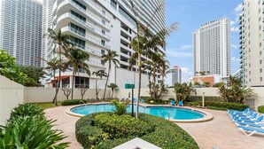A pool area with lounge chairs, palm trees, and high-rise buildings in the background. - Comfortable Apartment steps away from the beach (Hollywood)