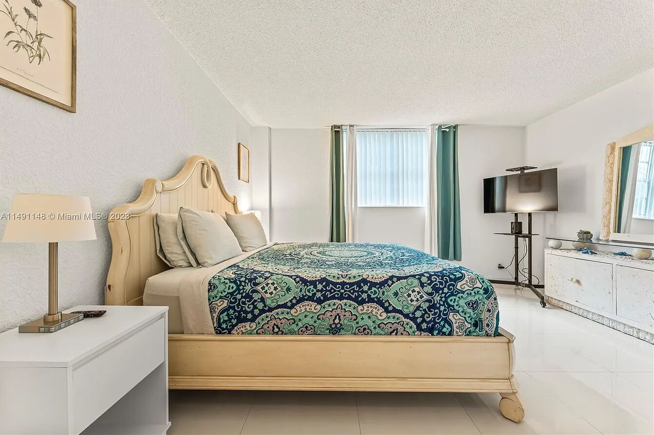 Een slaapkamer met een bed, nachtkastje, lamp, televisie en een dressoir.