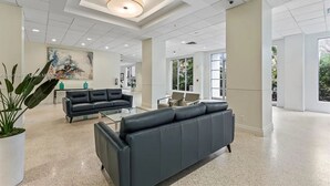 A spacious lobby with a modern design, featuring a large black leather sofa, a glass coffee table, and a potted plant. - Comfortable Apartment steps away from the beach (Hollywood)
