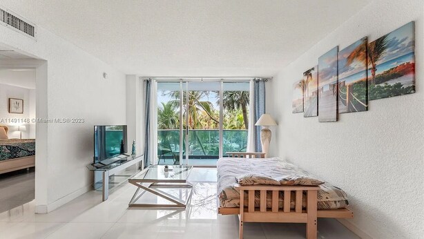A modern living room with a glass coffee table, a wooden bed, a TV on a stand, and a large window with a view of palm trees. - Comfortable Apartment steps away from the beach (Hollywood)