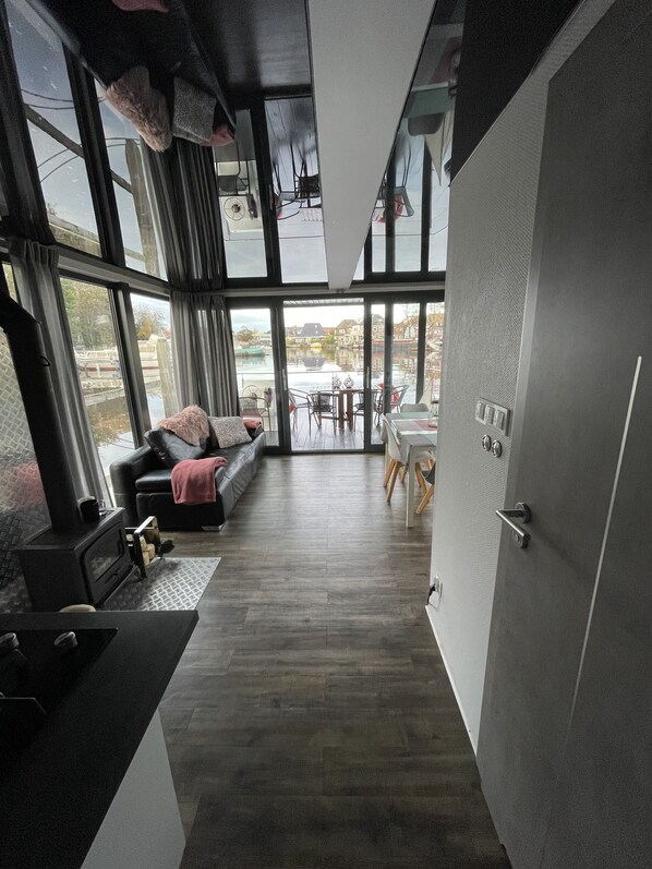 A modern interior with a sofa, dining table, and large windows offering a view of a canal.