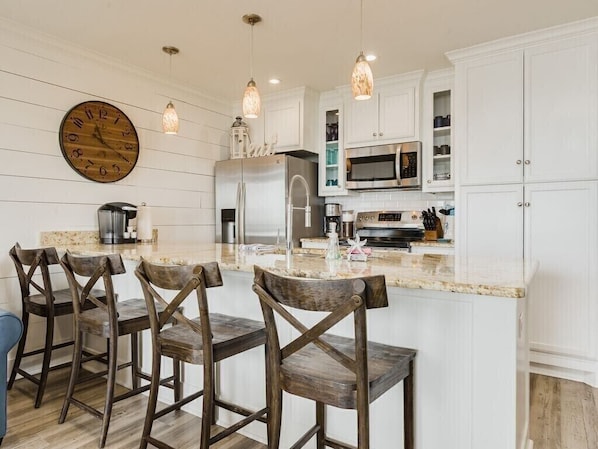 A kitchen with white cabinetry, a large clock, pendant lights, and a central island with bar stools.
